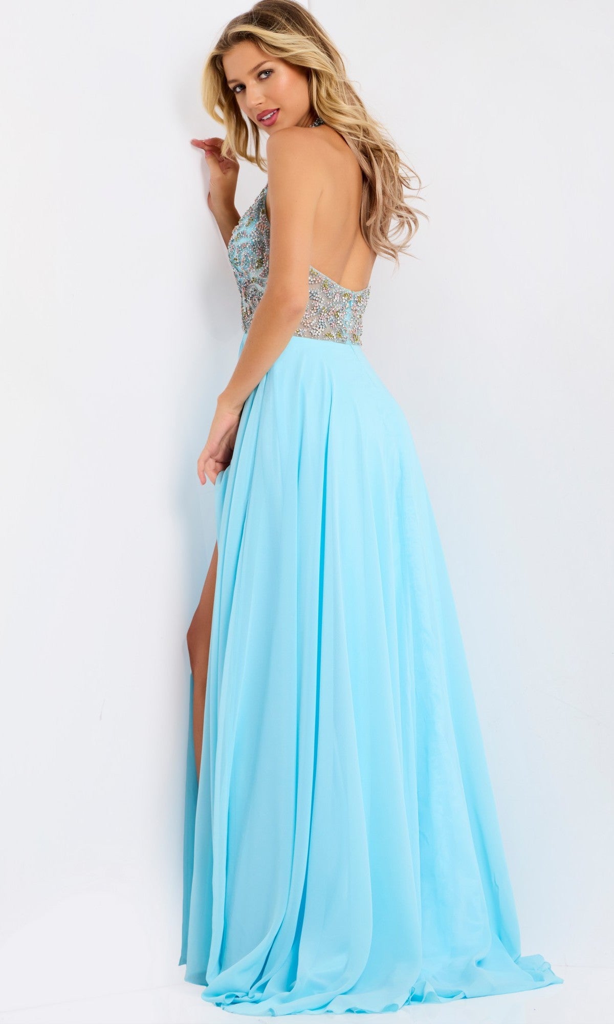 Woman wearing the Sheer Beaded-Halter Long Prom Dress (Jovani 48300) featuring a beaded halter bodice and flowing light blue skirt with a high slit, posing against a white background.